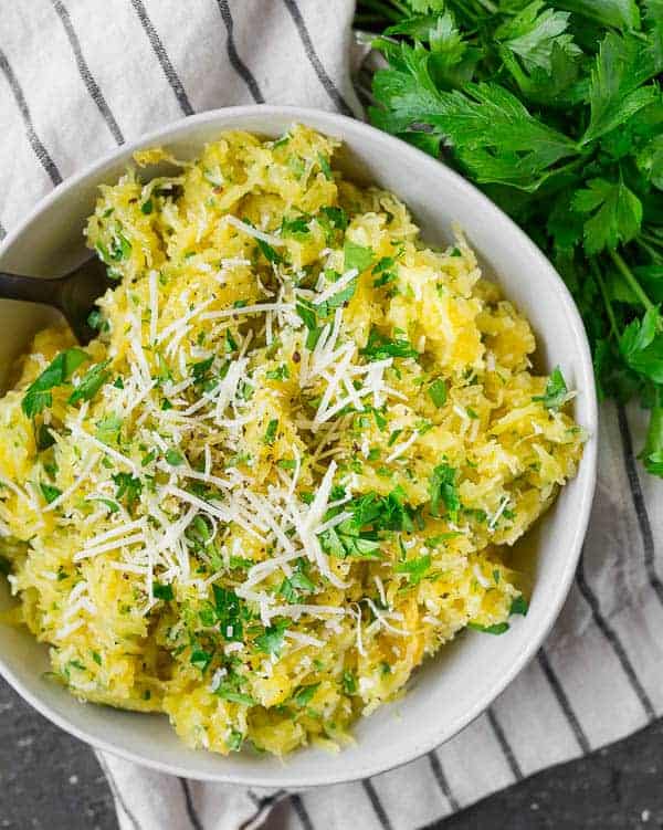 Overhead view of spaghetti squash sprinkled with fresh parsley and shredded parmesan cheese.