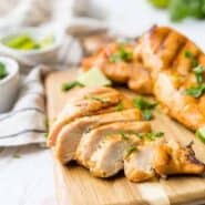 Grilled chicken breasts on a wooden cutting board. Chicken breast in the foreground is sliced.