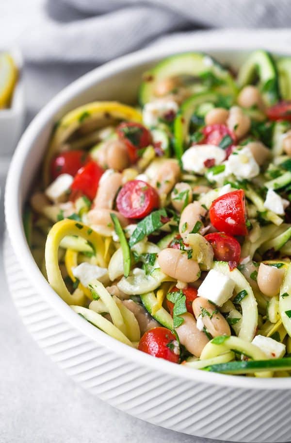 Close up view of zucchini noodle salad with lots of fresh green herbs, tomatoes, feta, and tomatoes.