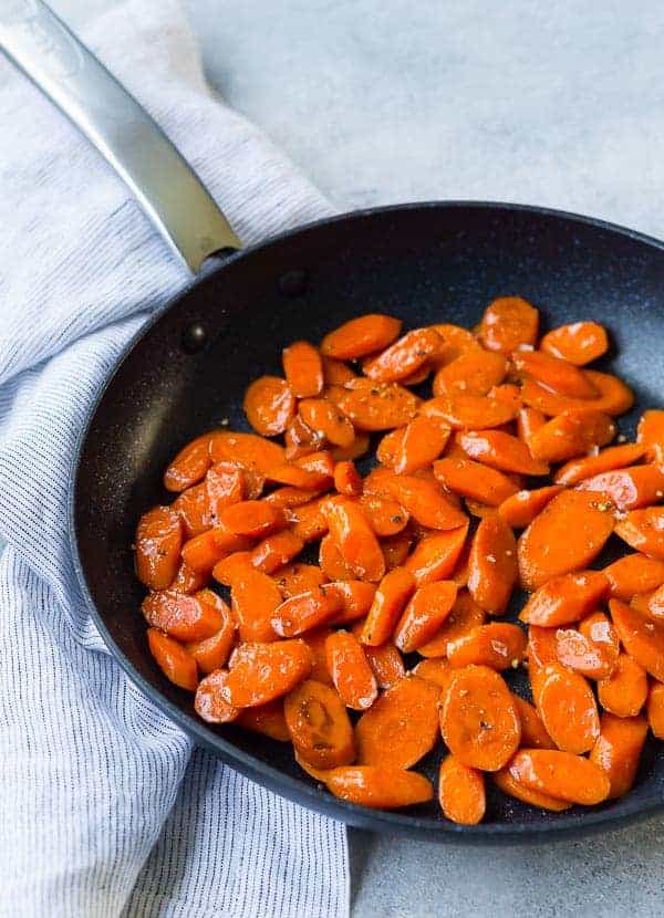 Black nonstick skillet with glazed sliced carrots in it.