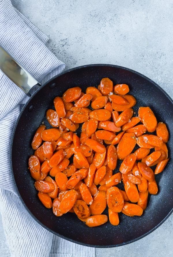 Black nonstick skillet with glazed sliced carrots in it.