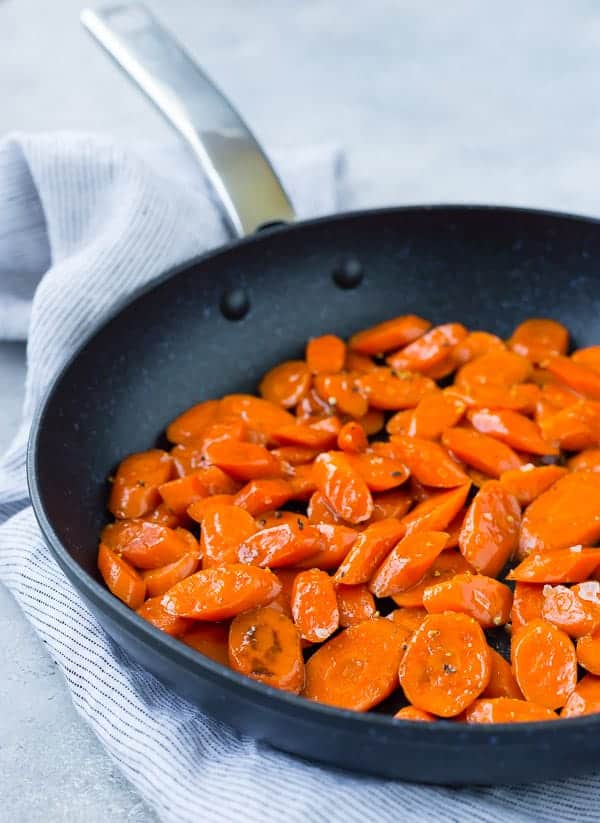 Black nonstick skillet with glazed sliced carrots in it.