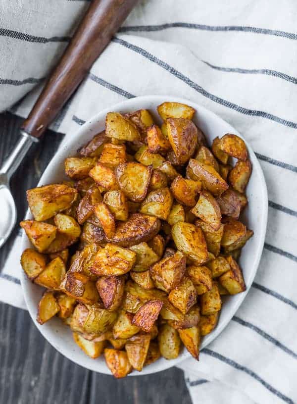 Overhead view of a oval white bowl filled to the brim with golden brown roasted potatoes.