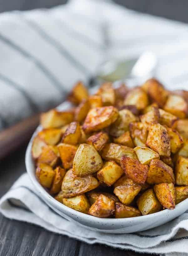 Close up view of small pieces of roasted potatoes in a small oval shaped white bowl.