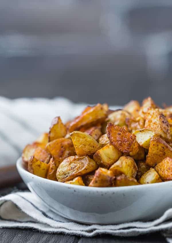 Close up view of roasted potatoes that are golden brown in color, placed in a small white bowl.