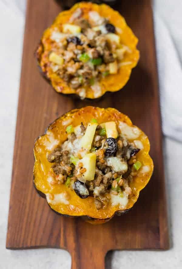 Overhead view of stuffed acorn squash halves lined up on a wooden serving platter.