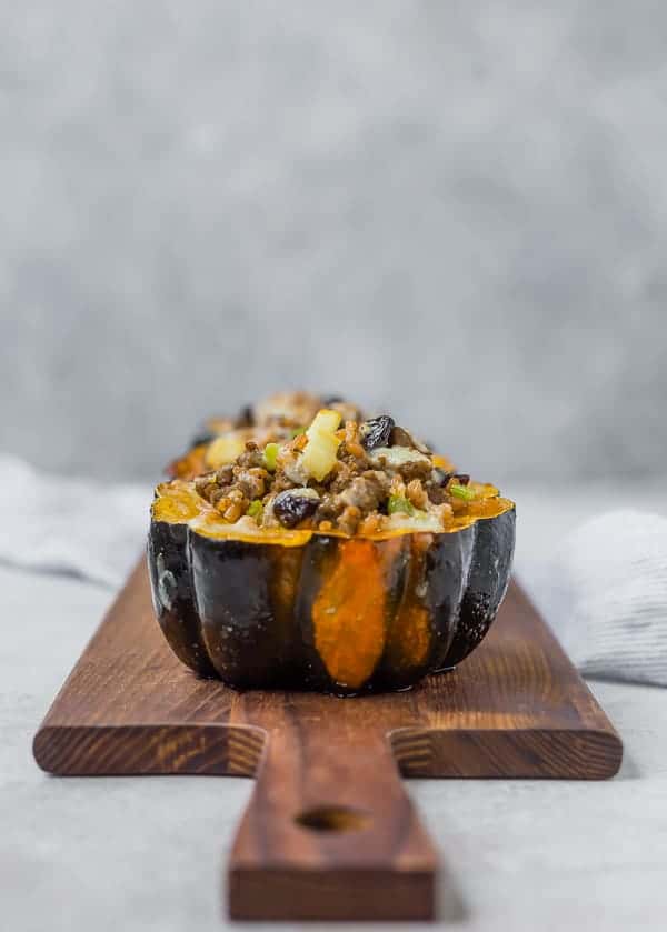 Acorn squash half filled with farro, sausage, dried cranberries, apples, and cheese on a wooden cutting board.