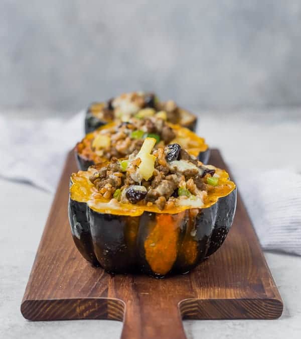 Stuffed acorn squash halves lined up on a wooden serving platter.