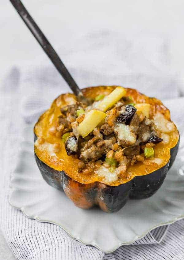 Stuffed acorn squash filled with farro, sausage, apples, and cheese on a white plate, with a fork stuck into the filling.