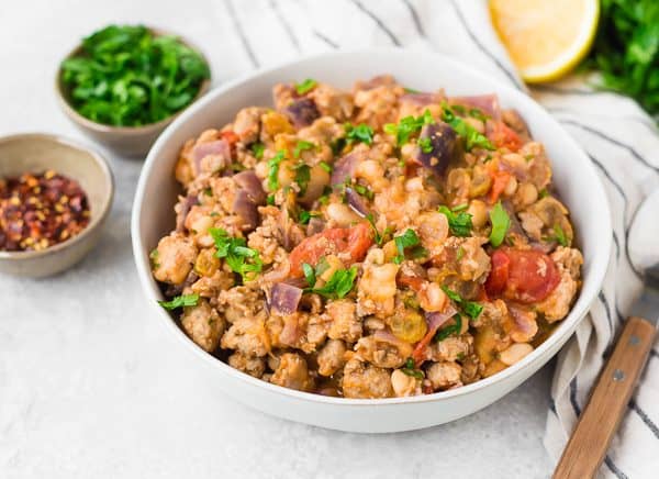 White bowl filled with sausage, tomatoes, red onions, and tomatoes. Sprinkled with fresh parsley. 