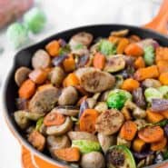 Sausage and vegetables in orange cast iron skillet.