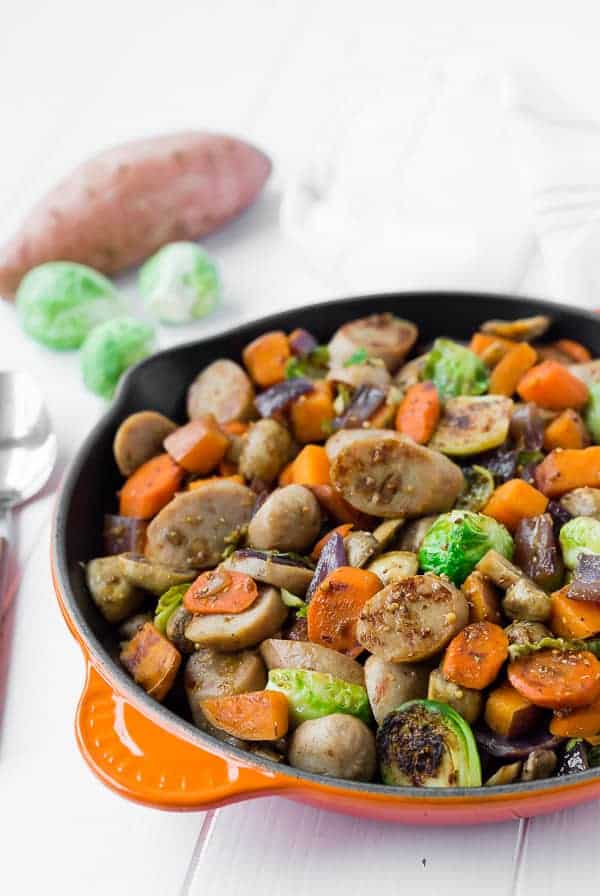 Image of sausage and fall vegetables in an orange cast iron skillet with brussels sprouts