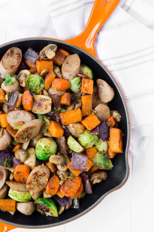 Overhead of sausage dinner in orange cast iron skillet.