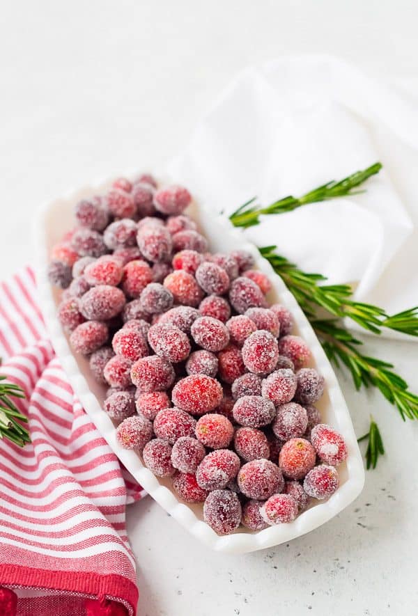 image of sugared cranberries in a glass white dish garnished with fresh rosemary