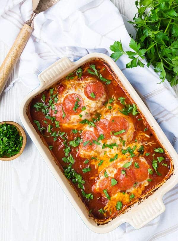 Overhead of baked chicken in rectangular baking dish garnished with parsley.