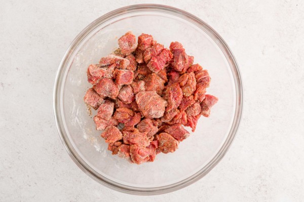 Chunks of beef in a glass bowl tossed with stew seasoning.