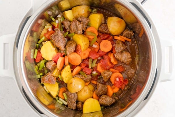 Vegetables, potatoes, and broth added to the Instant Pot along with browned beef chunks.