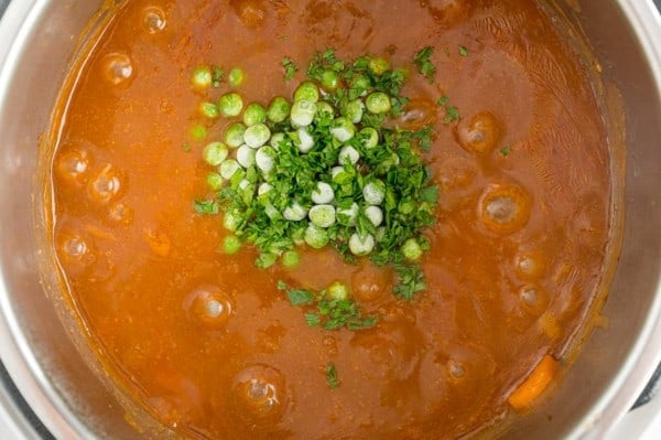 Frozen peas and chopped parsley added to beef stew inside the Instant Pot.