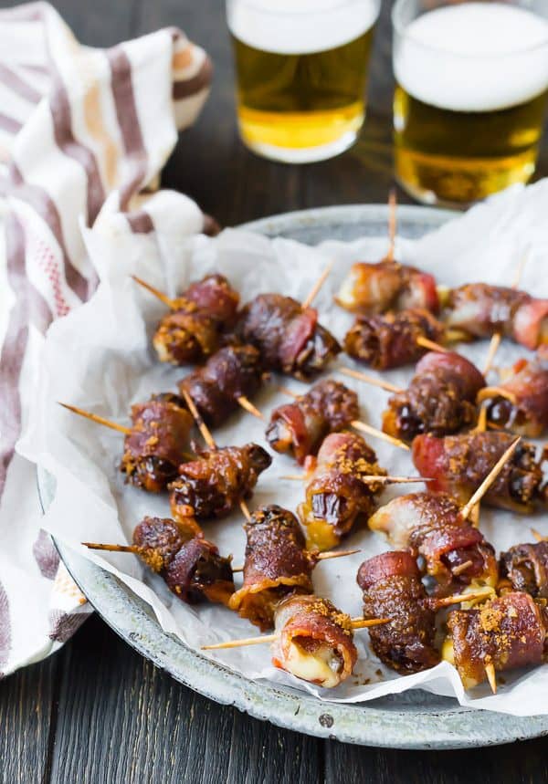 Image of bacon wrapped dates on crinkled parchment paper with two glasses of beer in the background. 