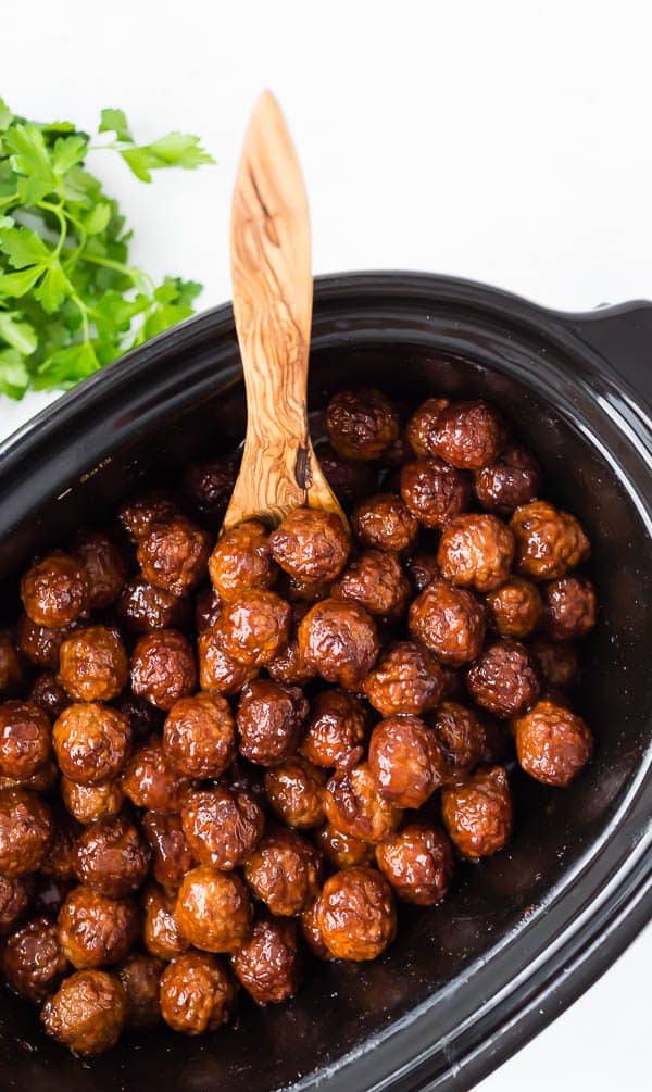 Overhead of meatballs in crockpot with wooden serving spoon.