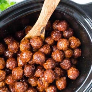 Image of crockpot meatballs with cherry bourbon sauce. Meatballs in slow cooker with wooden spoon, overhead shot.