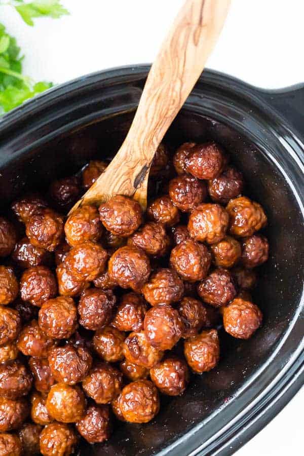 Crockpot Meatballs with Cherry Bourbon Sauce on RachelCooks.com Image of crockpot meatballs with cherry bourbon sauce. Meatballs in slow cooker with wooden spoon, overhead shot.