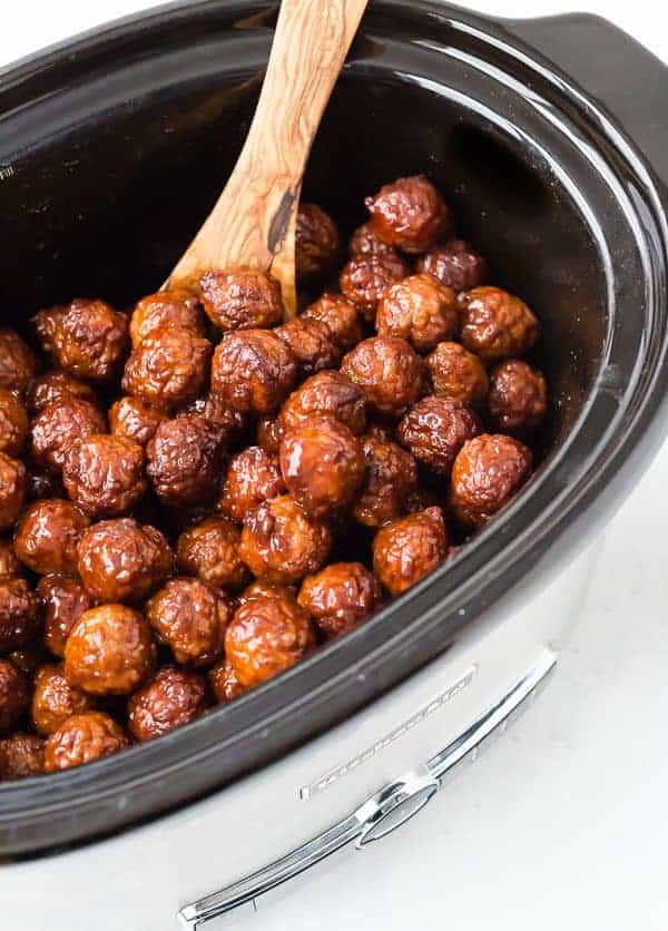 Closeup of meatballs in slow cooker with wooden spoon.