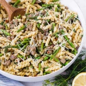 Image of lemon pasta in a white skillet with a wooden spoon. Garnished with lemon and dill.
