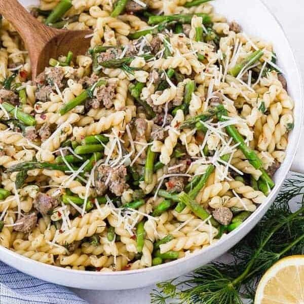 Image of lemon pasta in a white skillet with a wooden spoon. Garnished with lemon and dill.