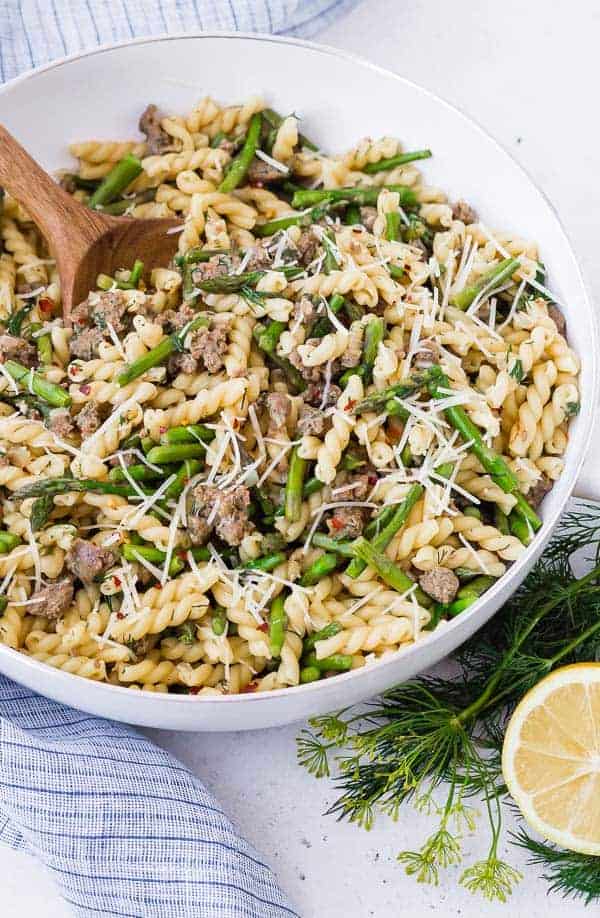 Lemon pasta in a white skillet with a wooden spoon. Garnished with lemon and dill. 