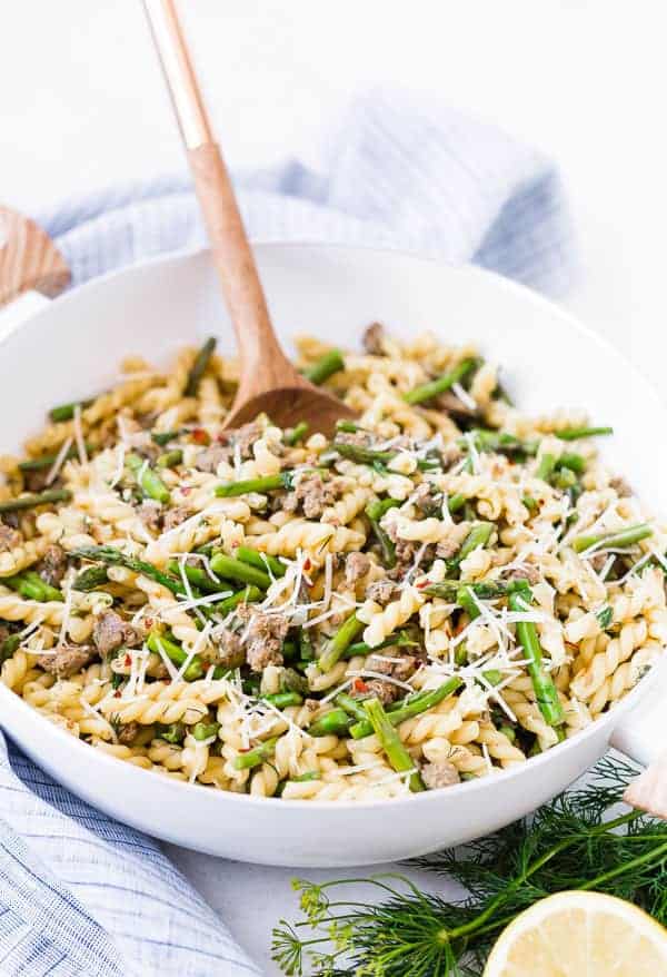 Pasta in shallow white serving bowl, with wooden spoon.