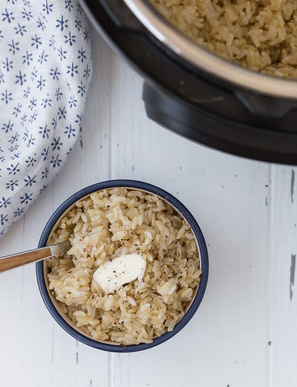 Image of Rice in a blue bowl with butter on top and a fork stuck in the bowl. An Instant Pot is in the corner of the image.