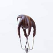 Image of Chocolate Cream Cheese Frosting on a electric beater attachment on a white background