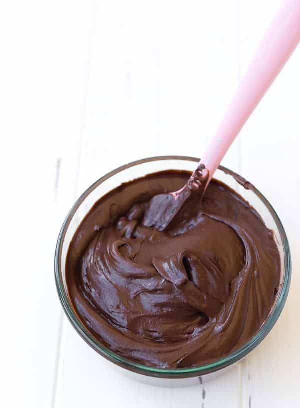 Overhead of bowl of frosting with pink scraper inserted.