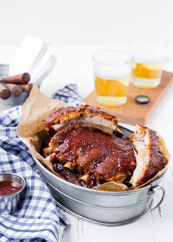 Prepared ribs, sliced into portions, in metal container with serving utensils nearby.