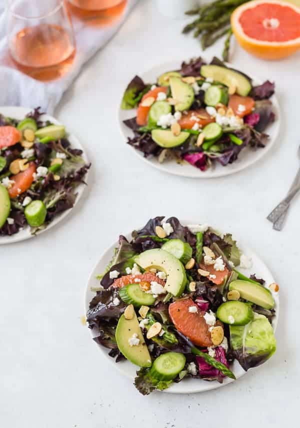 Three salads on white plates with wine glasses.