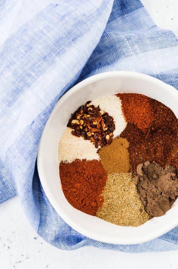 Spices in chili seasoning in a white bowl with a blue towel in the background. 