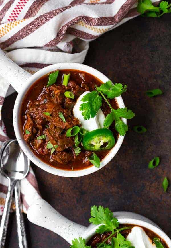 image of texas chili in a white bowl with a handle, garnished with sour cream, cilantro, and jalapeno