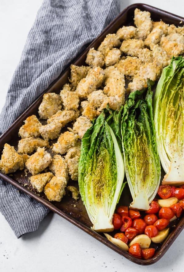 Image of sheet pan dinner with romaine, tomatoes, garlic, and crispy chicken. Shot from overhead. 