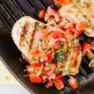 image of brushetta chicken with grill marks and bruschetta topping. Chicken is in a grill pan with two more chicken breasts.