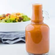 Image of homemade catalina dressing in a glass bottle with a taco salad in the background.
