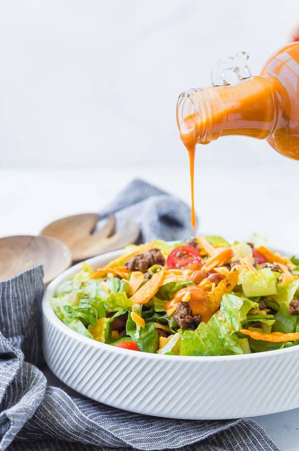 image of homemade catalina dressing being poured onto a taco salad