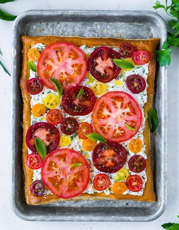 Overhead image of a tomato tart with varied colored tomatoes, fresh mint, and ricotta cheese.