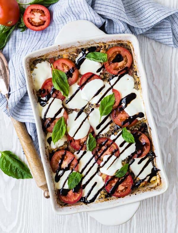 Overhead of chicken Caprese in white rectangular baking dish, garnished with fresh tomatoes, basil, mozzarella, and drizzled with balsamic glaze.