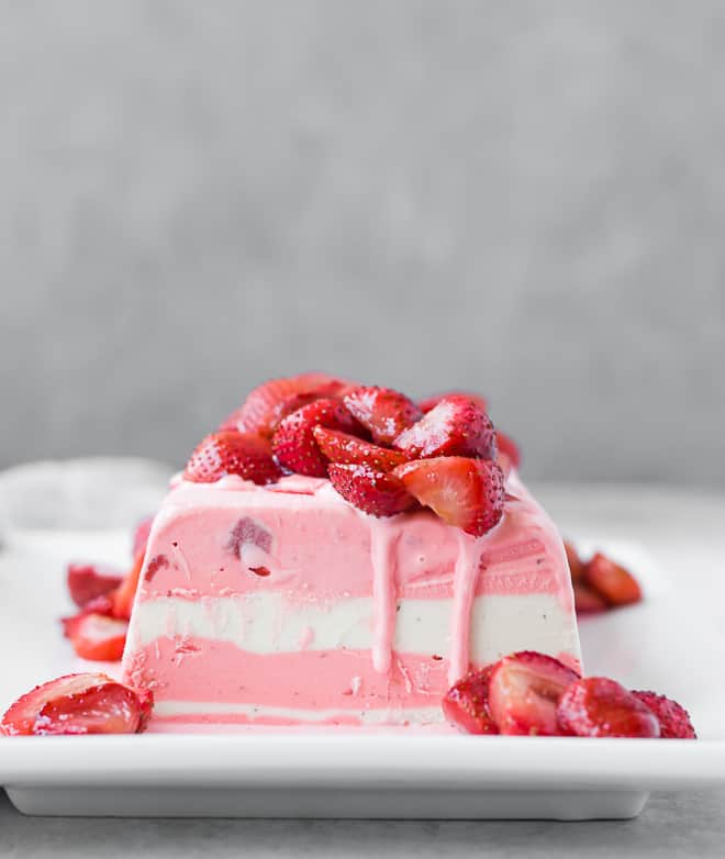 Image of ice cream terrine with layers of strawberry and vanilla ice cream. Topped with roasted strawberries that are still slightly warm, causing the ice cream to start to melt just slightly.