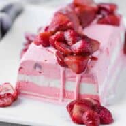 Image d'une terrine de crème glacée à la fraise et à la vanille étagée garnie de fraises rôties.  Disposé sur une plaque rectangulaire blanche.
