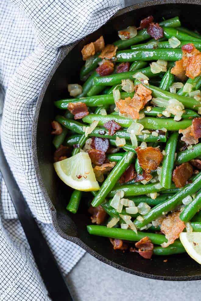 Overhead view of green beans and bacon in a black skillet.