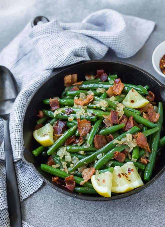 green beans with bacon in a cast iron skillet, garnished with lemon wedges