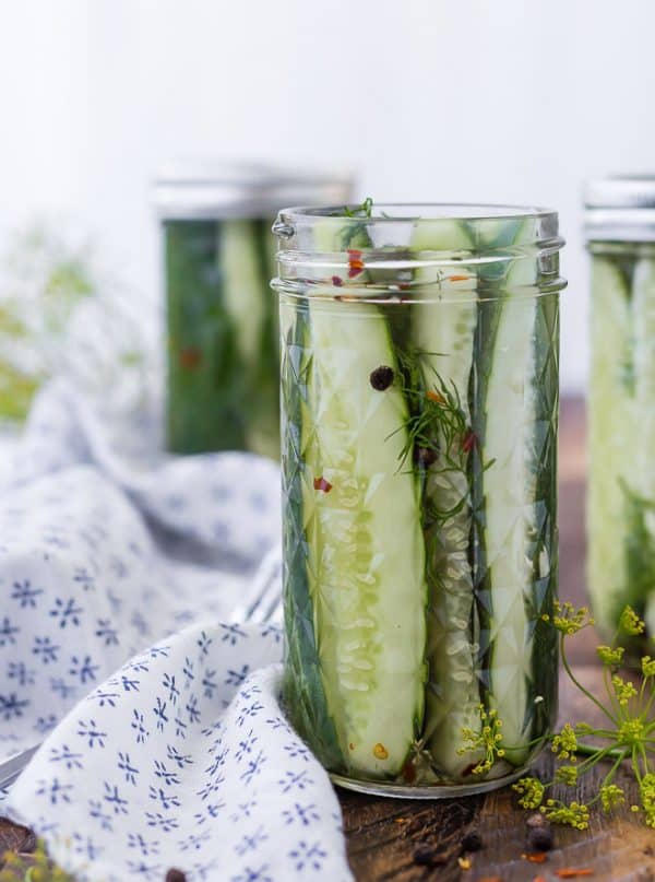 Image of homemade refrigerator dill pickles in a jar. Two jars in the background. Sprigs of dill also pictured.