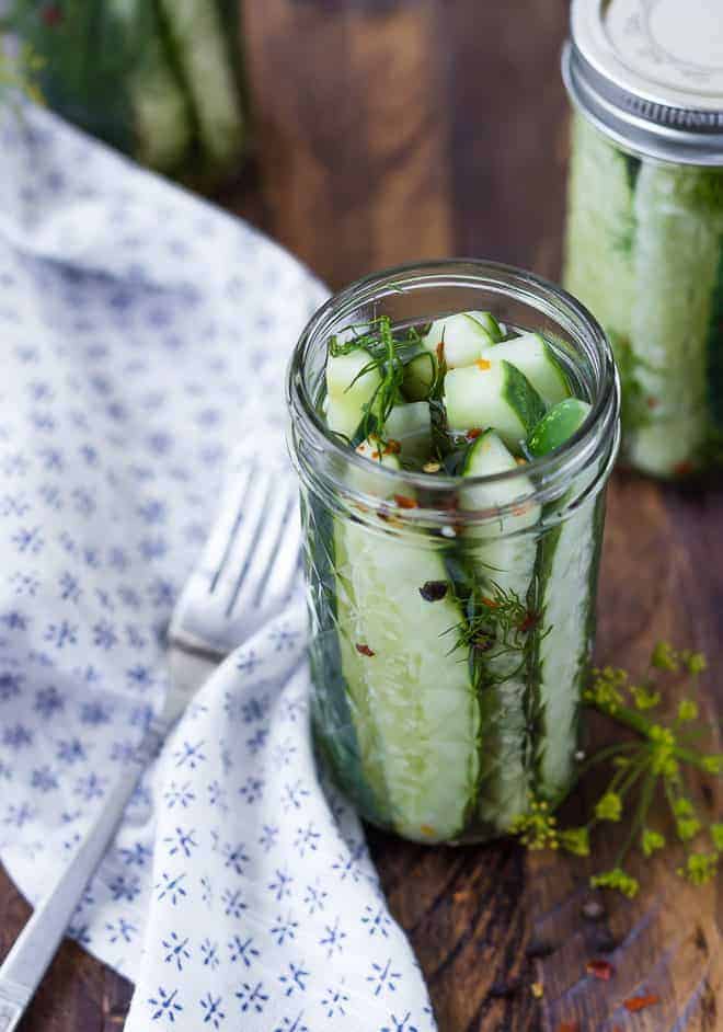 Pickles in slim glass canning jar without lid. Another jar in background.